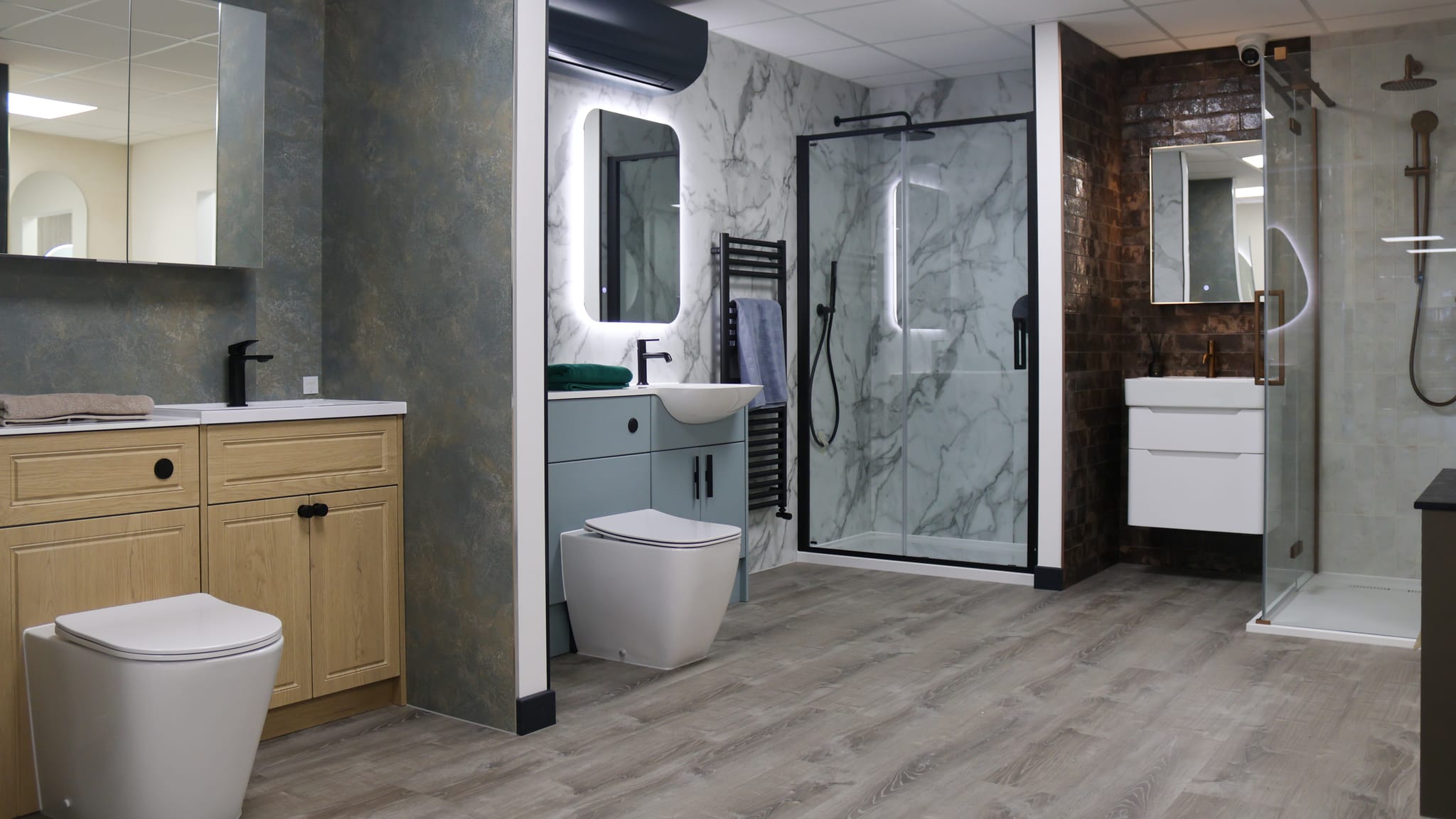 Bathroom displays at Pochin Eastbourne: oak and sage vanity units, a back-lit mirror, black-framed shower enclosure and corner shower
